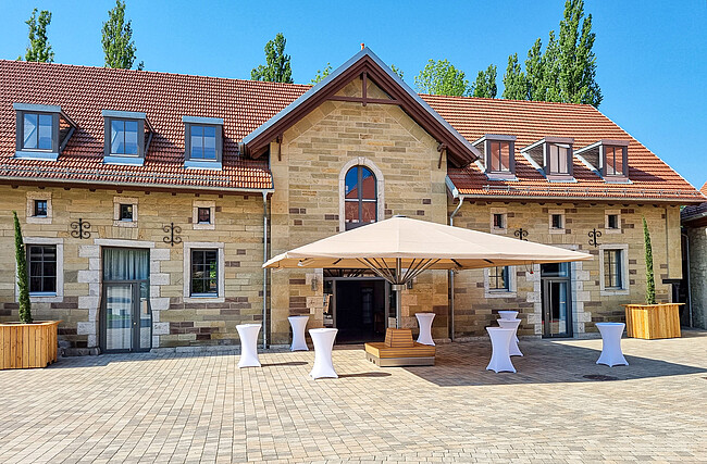 Außenansicht vom Gebäude Alter Speicher der Eventlocation Gut Wöllried mit Sonnenschirmen und Cocktailtischen im Sommer