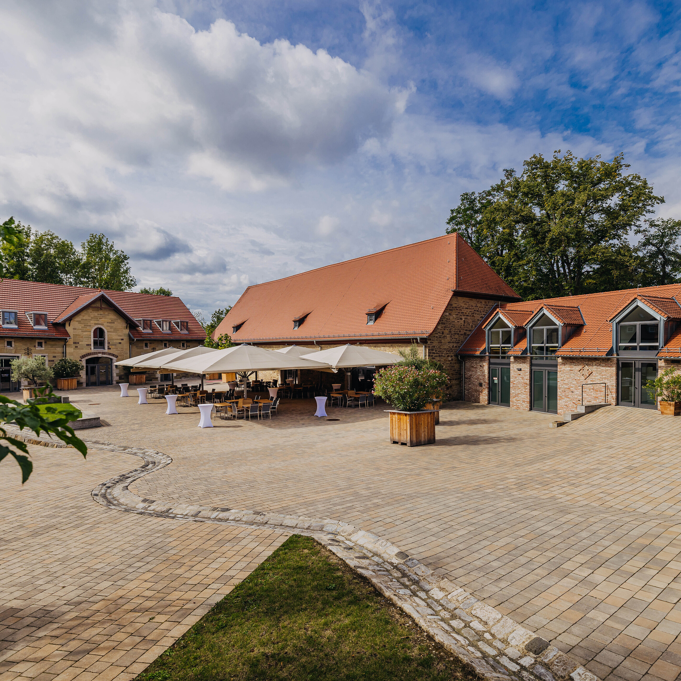 Große Festscheune und weitläufiger Innenhof der Eventlocation Gut Wöllried in Würzburg mit Sonnenschirmen für ein Sommerevent