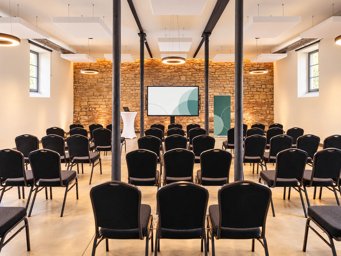 Konferenzraum im Alten Speicher auf Gut Wöllried mit Reihenbestuhlung, Präsentationsbildschirm und historischer Natursteinwand