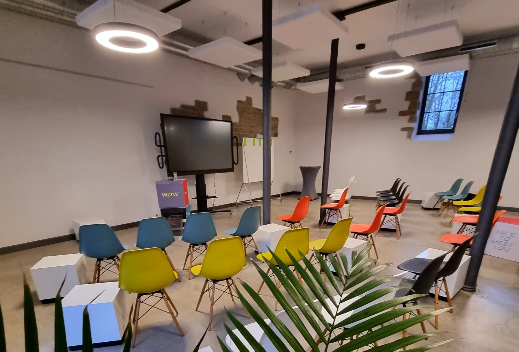 Kreativer Workshopraum im Alten Speicher auf Gut Wöllried mit farbigen Stühlen, Präsentationsbildschirm und flexibler Bestuhlung